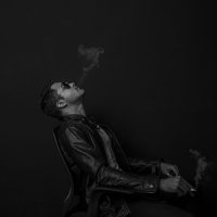一位穿着深色衬衫的男性在通勤地铁上低头看着手机屏幕，耳机线垂在胸前，正在记录广播剧平台试听长度的实测结果